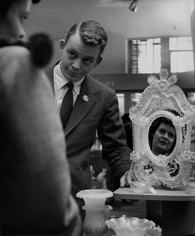 A woman looking at her reflection in the mirror in front of a young salesman.