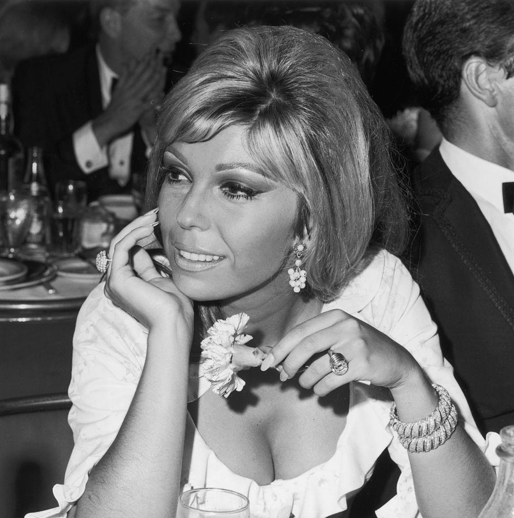 Nancy Sinatra sitting and holding a flower at a Cocoanut Grove opening, Los Angeles, 1966.