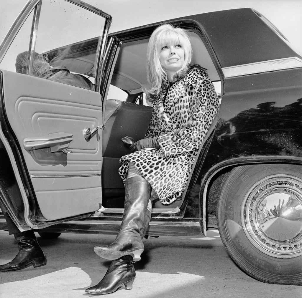 Nancy Sinatra gets out of a car wearing a leopard skin coat and knee length boots, 1966.