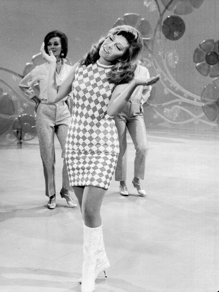 Nancy Sinatra performs on stage, with backup dancers and a floral backdrop, 1969.