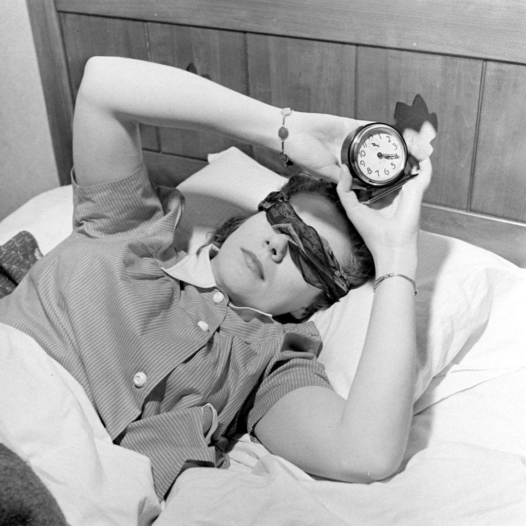 Radio announcer Jean Ruth Hay holding an alarm clock while lying on the bed, Salt Lake City, 1942.