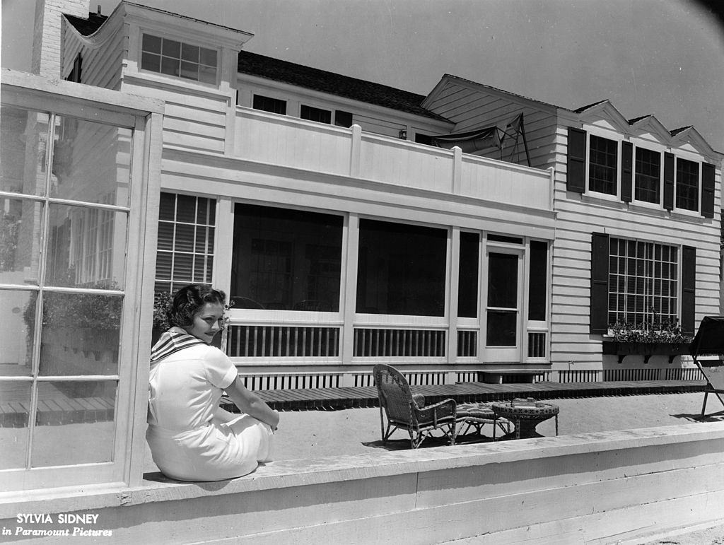 Sylvia Sidney is perched on a ledge by her garden, 1932.