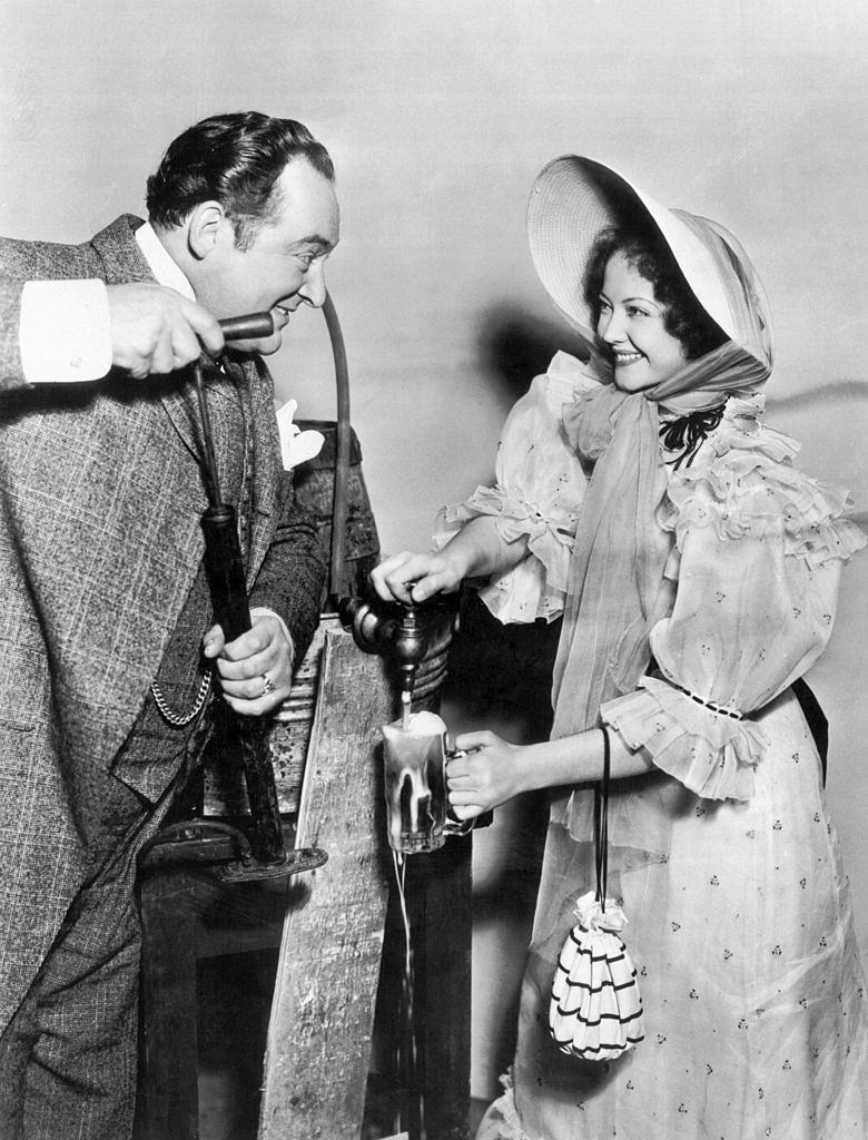 Sylvia Sidney tapping a stein of beer for Edward Arnold as he pumps, 1933.