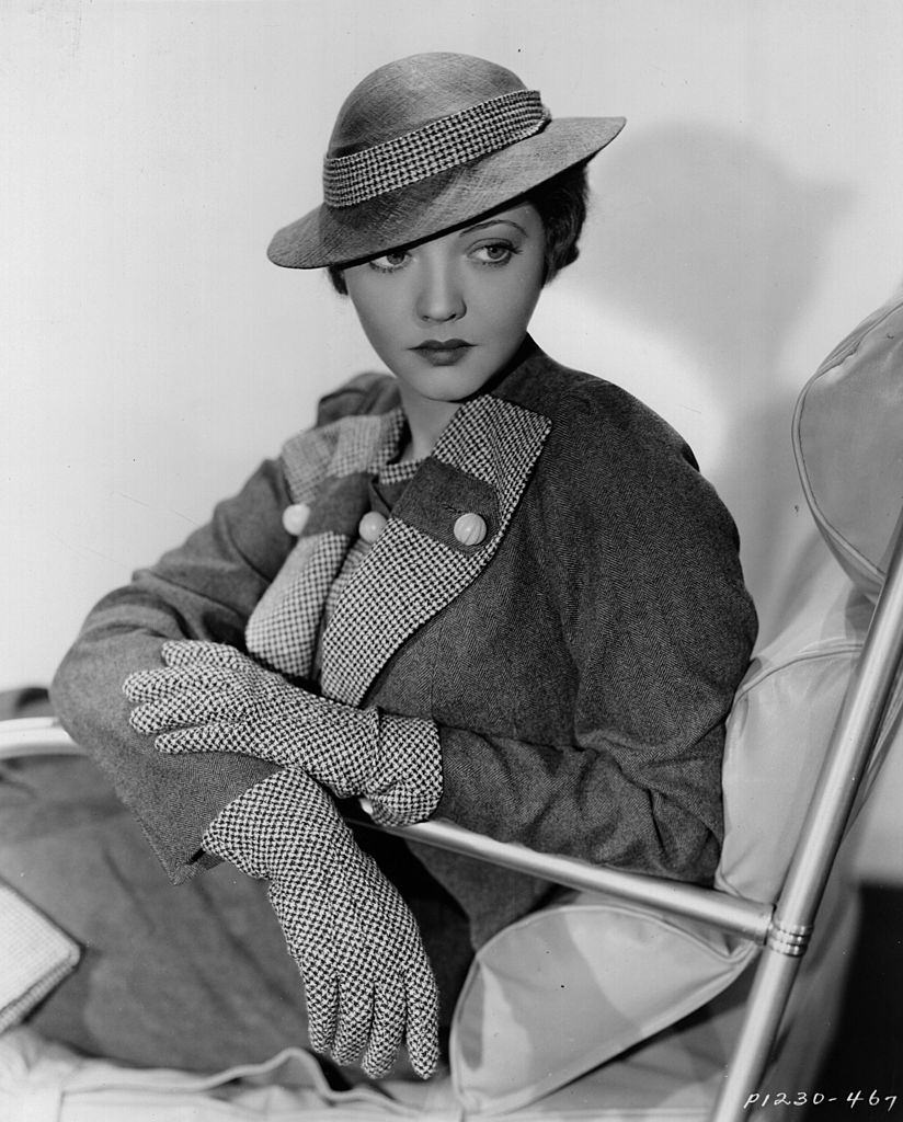 Sylvia Sidney wearing a street suit in brown worsted with vest, lapels, gloves, handbag and hat band in brown and white check, 1934.