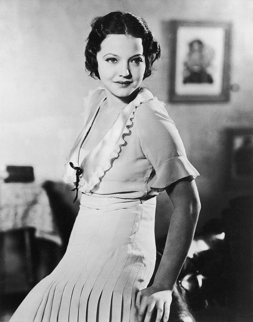 Sylvia Sidney wearing a pleated dress, leaning against the back of a sofa, 1935.