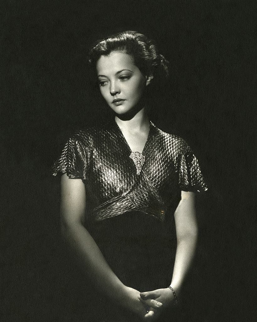 Sylvia Sydney, with dark hair combed in an upsweep style, wearing a glittery dress with a broach, 1935.