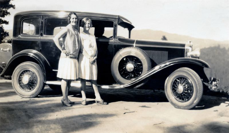 Two elegant ladies with bob hairdos posing with a 1930 Viking Eight Sedan on a dirt road in the countryside, 1930