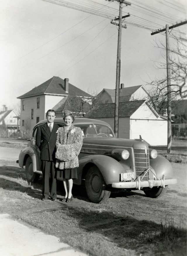 A lady dressed in a fur coat and a fellow in a double-breasted suit posing with a 1937 Oldsmobile Eight on a sunny winter's day.