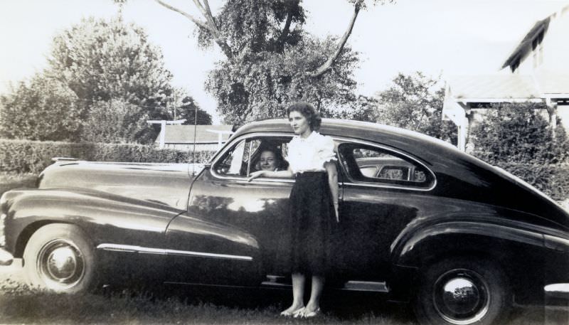 A fashionable brunette lady posing with a 1947 Oldsmobile Dynamic Cruiser in summertime, 1948
