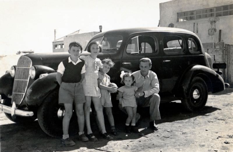 A father and four of his children posing with a 1935 Oldsmobile 4-Door Touring Sedan in bright mid-day sunshine, Israel, 1950
