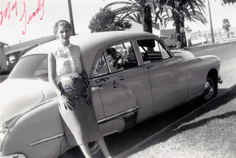 A young blonde lady posing with a 1949 Oldsmobile 88 4-Door Sedan on a sunny day.