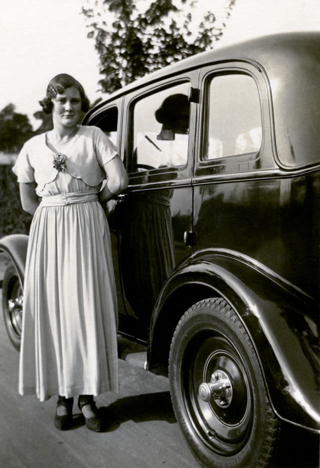 An elegant young lady in an ankle-length gown posing with an Oldsmobile on a gravel road in the countryside, Nuremberg, June 13, 1934