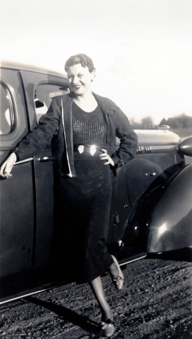 A stylish lady dressed posing with a 1936 Oldsmobile Eight on a gravel road in late afternoon sunshine, 1938