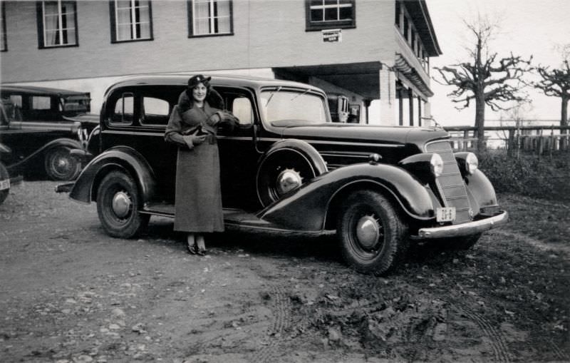 An elegant young lady in a fur-collared coat posing with a 1934 Oldsmobile Eight on a bleak winter's day, 1938