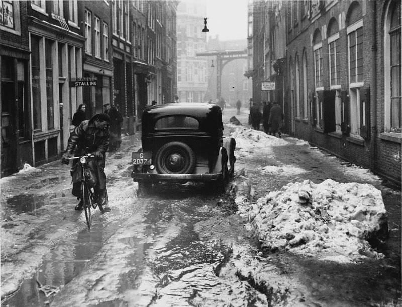 Thaw in Amsterdam, car passes cyclist in the Staalstraat. Amsterdam, March 11, 1947