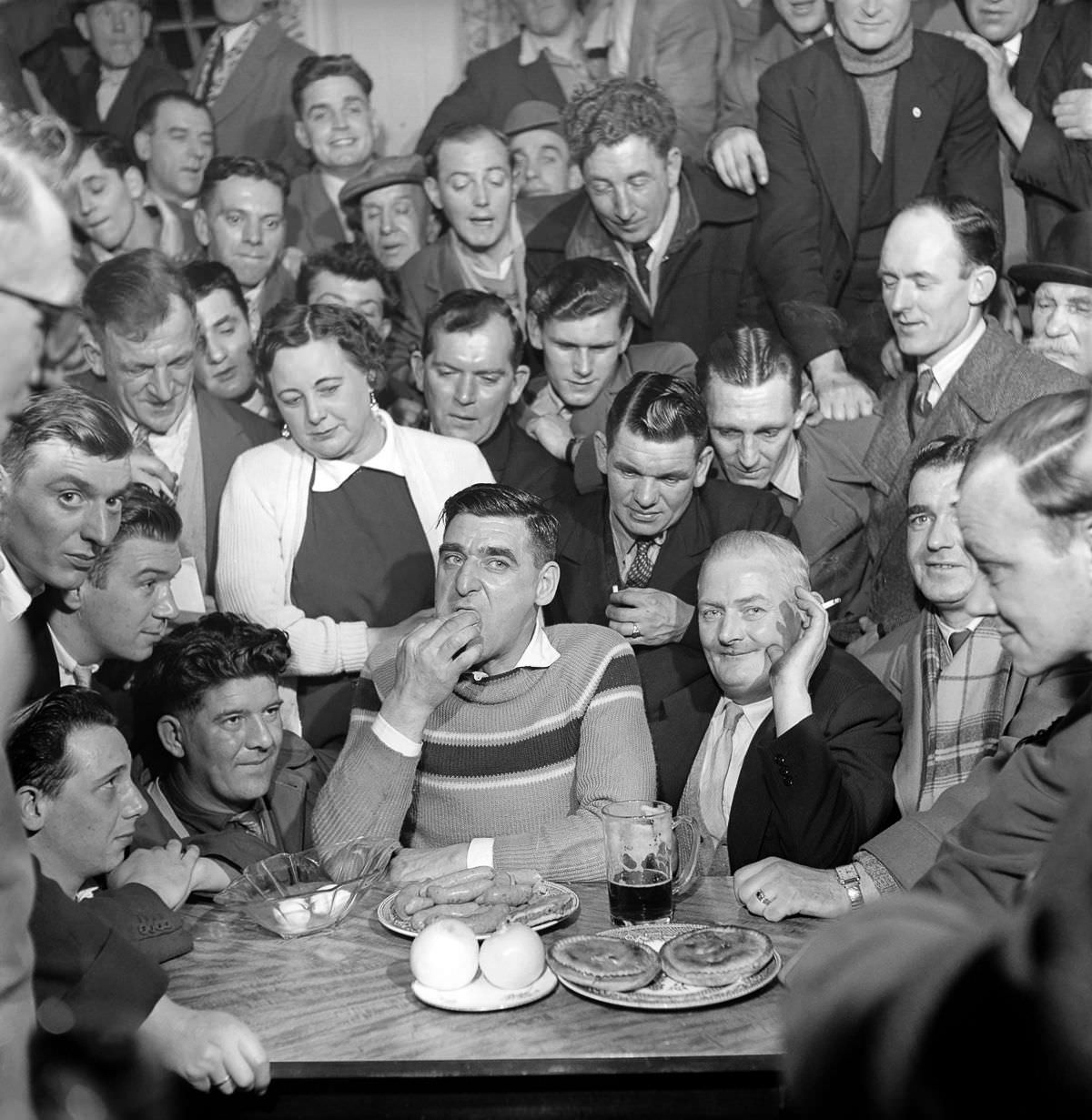 Spectators look on as Joe Steele takes part in a food-eating competition, 1958.