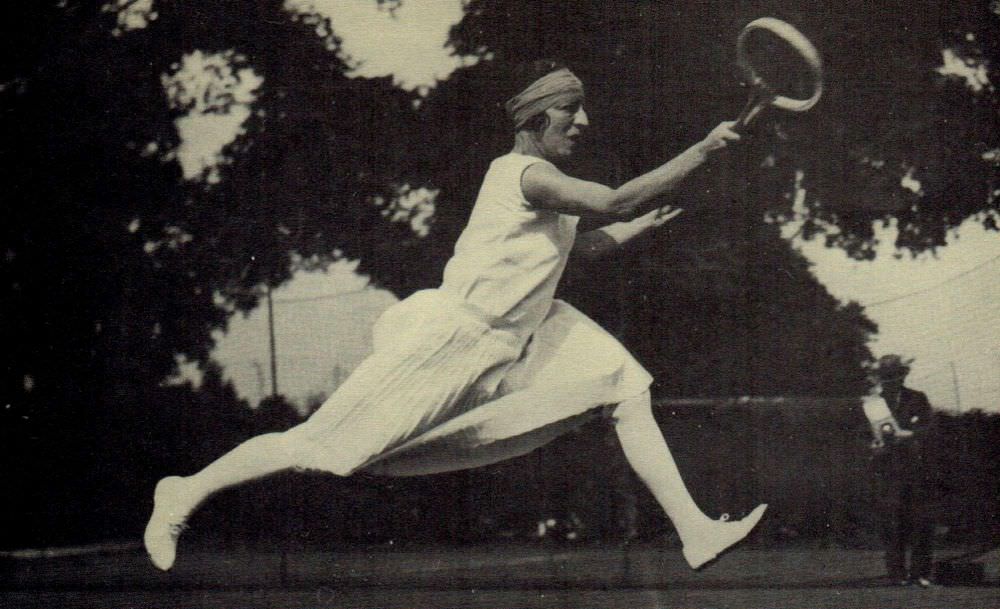 French tennis player Suzanne Lenglen can be seen wearing a Patou outfit and her trademark bandeau headwear, which became part of mainstream fashion in the 1920s.