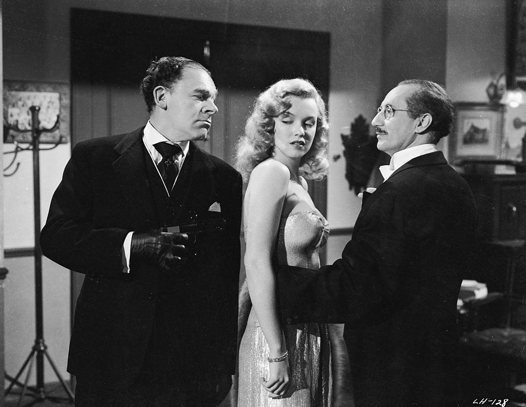 Marilyn Monroe with Groucho Marx and fall foul of a man with a gun in a scene from 'Love Happy', 1949.