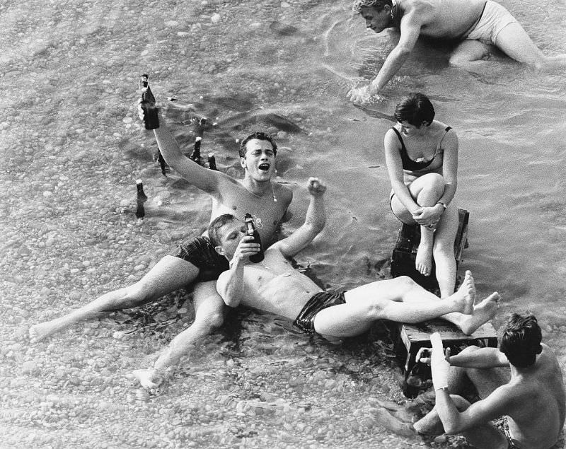 A group of young people lying in shallow water and drinking beer.