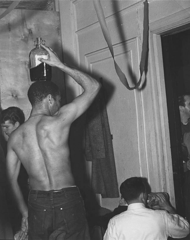 A man holding a bottle of wine on his head at a party in Greenwich Village.