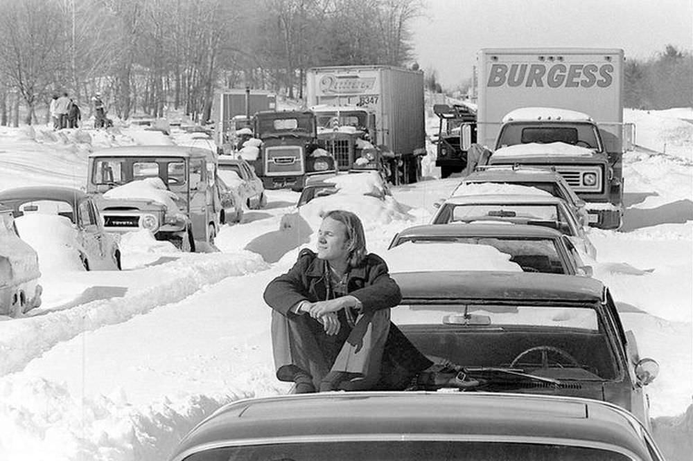 Roy Sodersjerna of Higham, Mass. suns himself on the hood of his car which is stuck in snow on Massachusetts Route 128 in Dedham on Feb. 9, 1978.