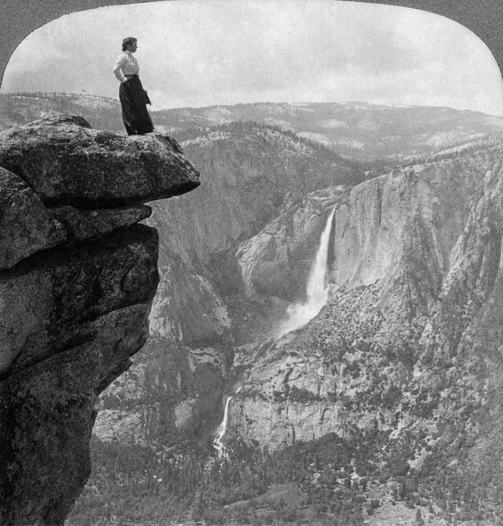 A tourist stands on Glacier Point with Yosemite Falls in the background, 1902.