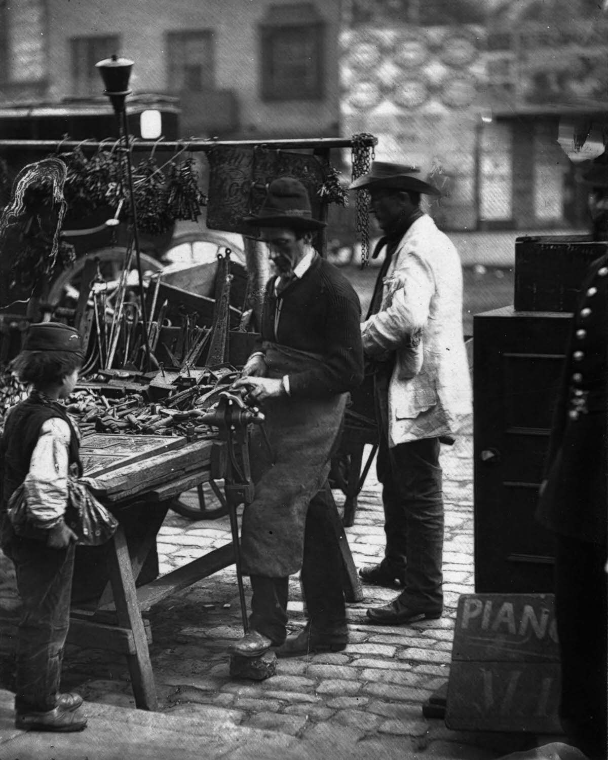 A locksmith mends locks at his stall, 1877.