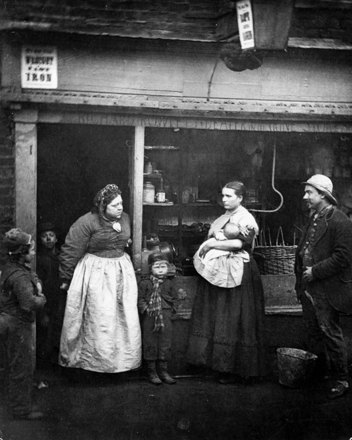 People in front of a rag shop in Lambeth, London, where the Thames annual tidal overflow causes hardship to the locals, 1877.
