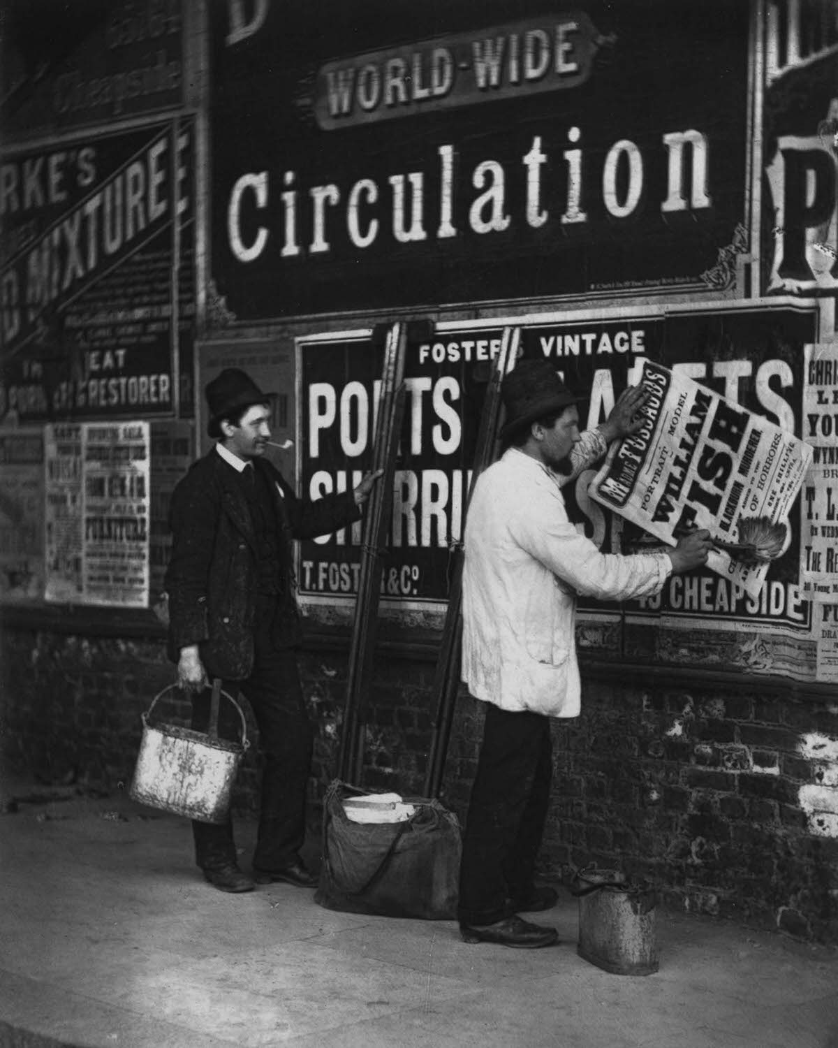 Bill stickers paste placards advertising Madame Tussaud’s waxworks museum, 1877.