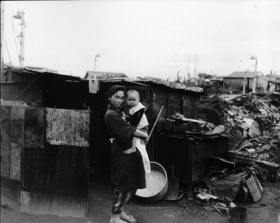 A mother visibly grateful to be alive holds her child outside of their Ebisu home on a rubble-strewn block. 1945. Tokyo, Japan.