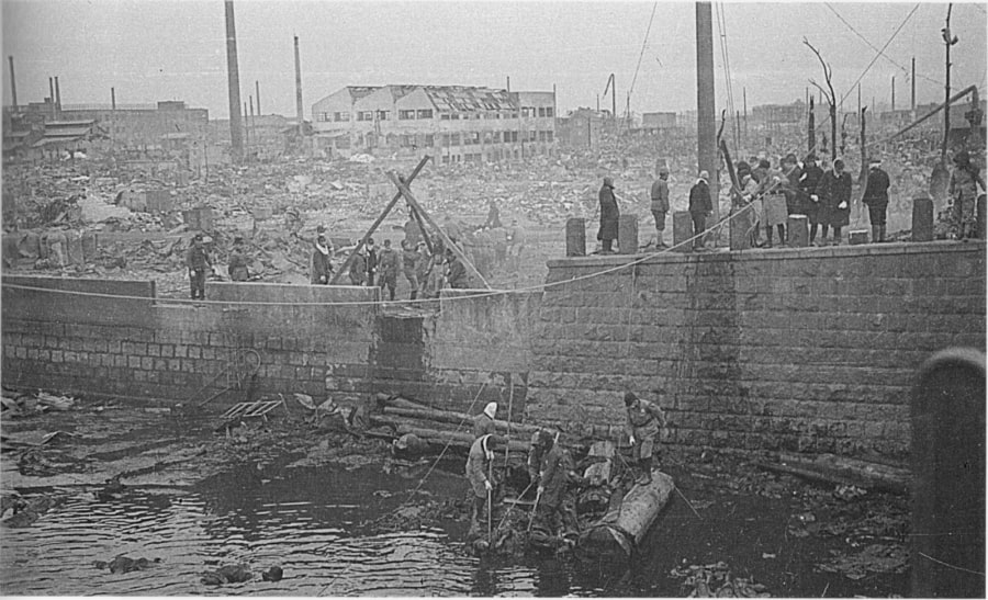 Civilians and first responders attempt to salvage the drowned, burned, or asphyxiated victims of the Tokyo bombing out of the river. The riverbank seen here is a stone's throw away from the Kikukawa Bridge in Tokyo's exchange district. March 16, 1945. Tokyo, Japan.