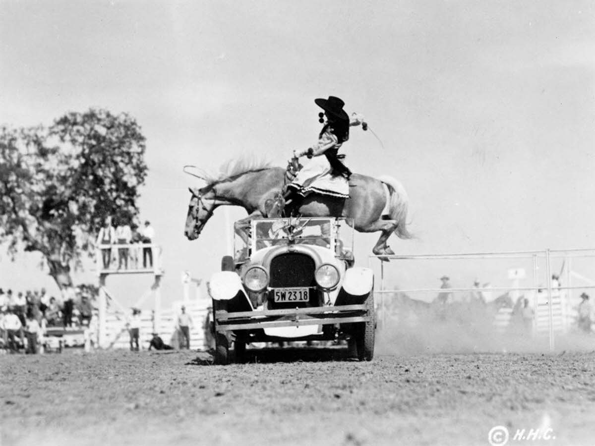 A woman and her horse hurdle a convertible at a California rodeo. 1934.
