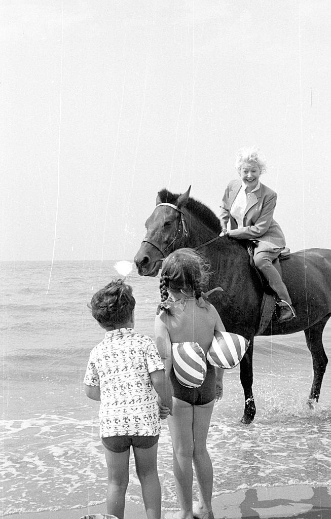 Marianne Lincoln, who will compere the 'Stars At Blackpool' television show, enjoying a horse ride on the beach where she meets two young fans, 1953.