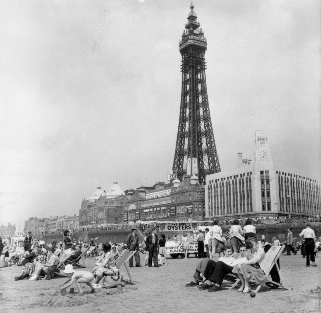 Blackpool Tower behind holidaymakers relaxing on the beach of the famous Lancashire resort, 1953.