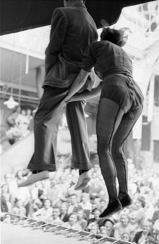 A member of the audience, held by the seat of his pants by a performer, jumps up and down on a trampoline in front of the crowd at the famous seaside resort of Blackpool, 1953.