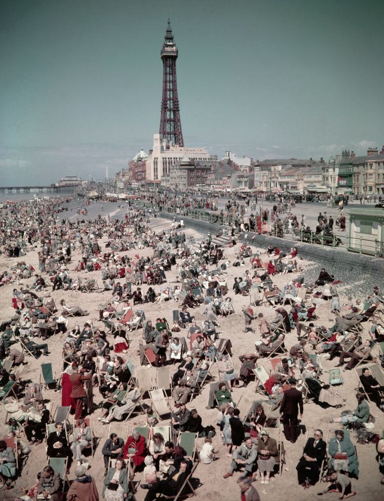 Holidaymakers and visitors, many seated in deck chairs, enjoy a day on the beach at the seaside resort of Blackpool in Lancashire in August 1952.