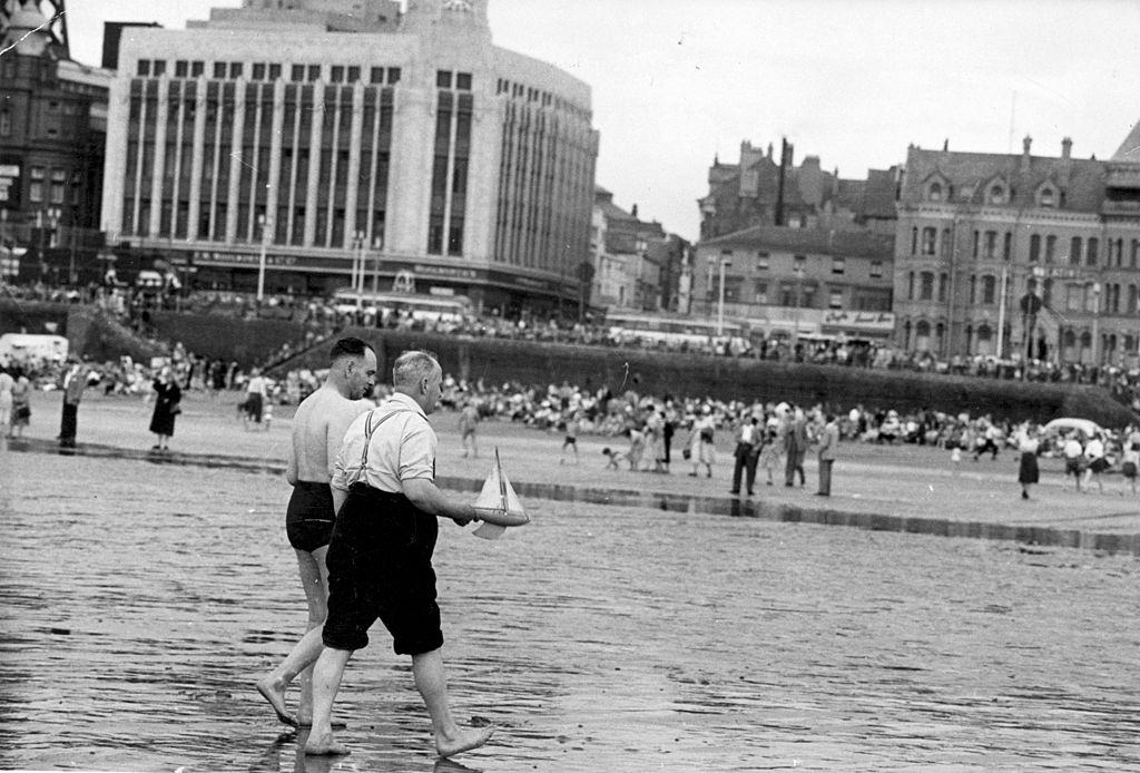 Two men with their toy boat on the beach at Blackpool, July 1956.