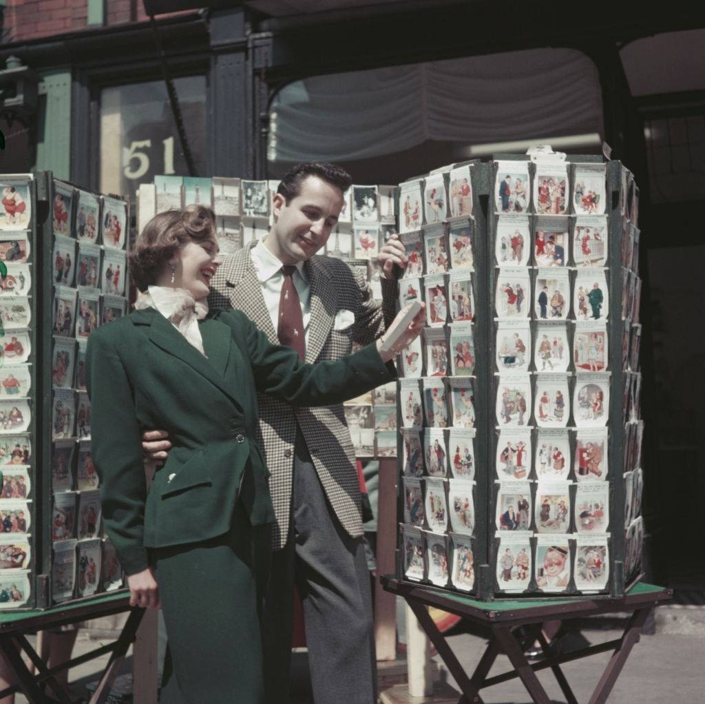 A young couple laugh as they view a carousel of saucy postcards at a postcard shop in the seaside resort of Blackpool, Lancashire in July 1954.