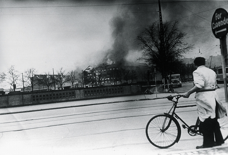 Cyclist looking at the burning Shellhouse (Getapo's head quarter) after the RAF attack.. 18th April 1944.
