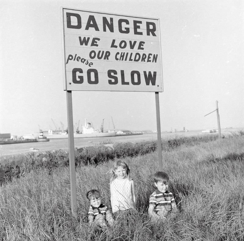 Children under a sign designed to protect them on the Pigeon House Road, Ringsend, Dublin, 1969