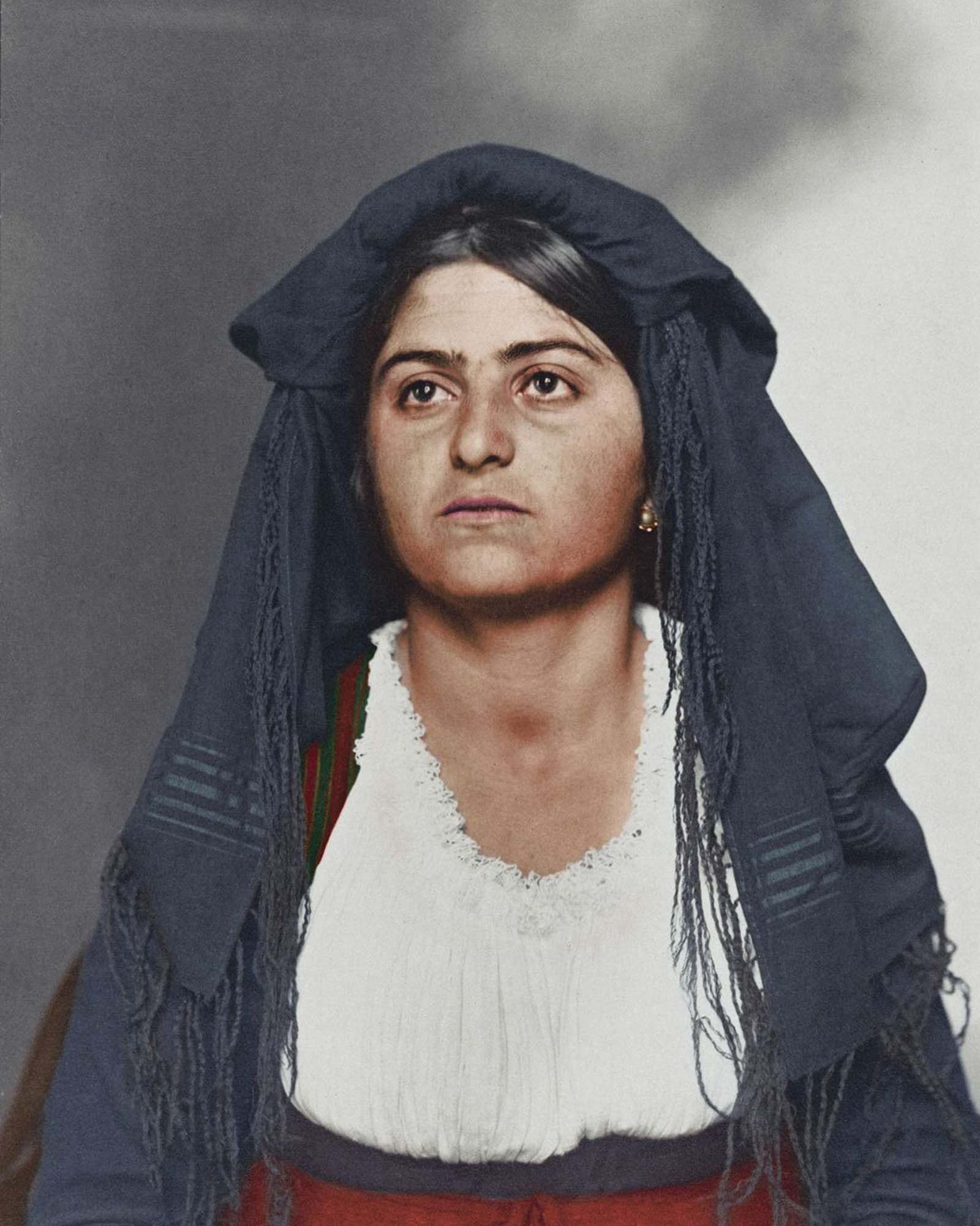 Italian woman.” This traditional dress was most likely homespun and consisted of a long, wide dress to cover the ankles. Above, a bodice and sleeves were tied in such a way to expose portions of the linen blouse. Colors and materials were usually regional. Shawls and veils were also a common feature