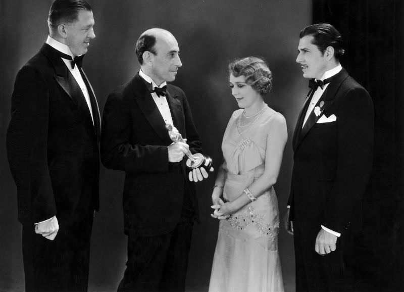 William C Demille, President Of The Academy Of Motion Picture Arts And Sciences hands an Oscar to Mary Pickford (with Warner Baxter and Hans Kraly looking on) at the first ceremony in 1929