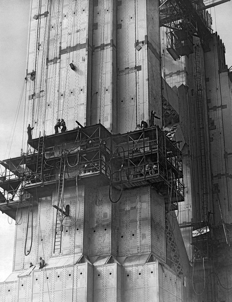 The Golden Gate Bridge under construction with riveters at work in cages on the South Tower, 1935.