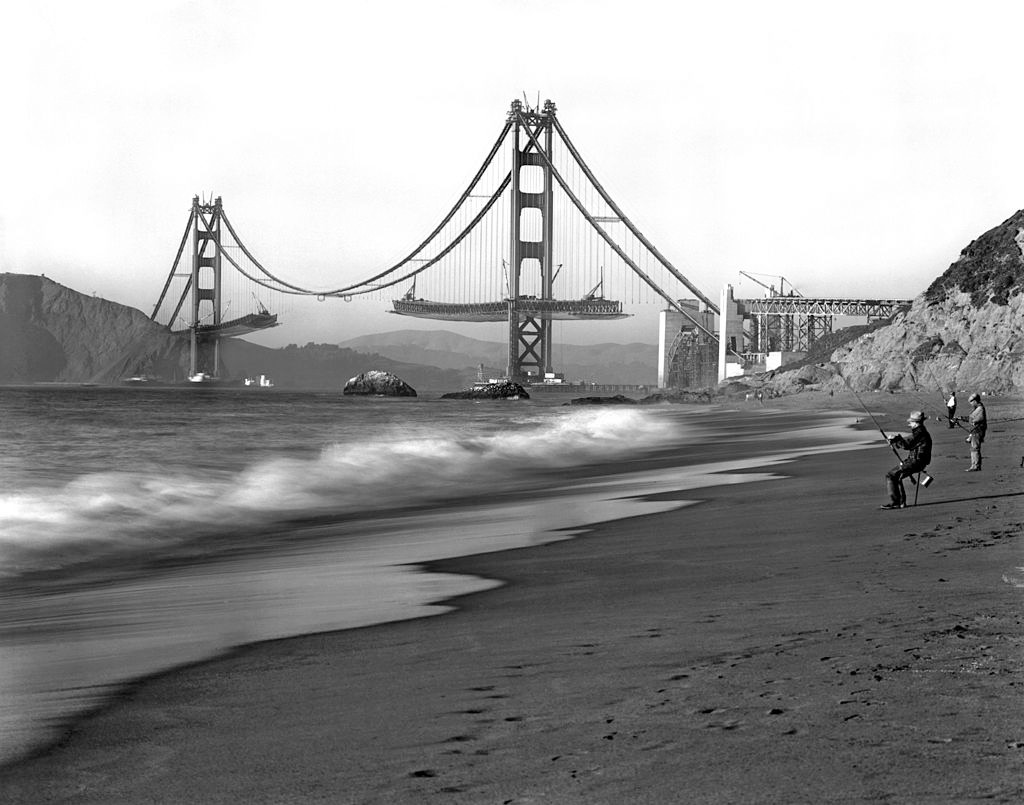 Fishermen on Baker Beach enjoy the view of the Golden Gate Bridge under construction, 1936.