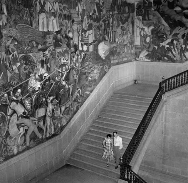 A young couple walk down a staircase in a monumental building in Mexico City.