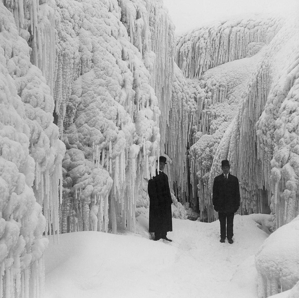 Two men pictured standing among the crystal corridors and caves of a frost-bound Niagara, 1950.