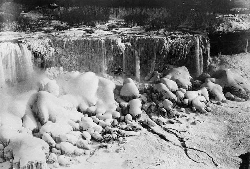 A Bell Aircraft helicopter flies close to Niagara Falls, which is frozen. Only a trickle of water is coming from the falls, 1951.