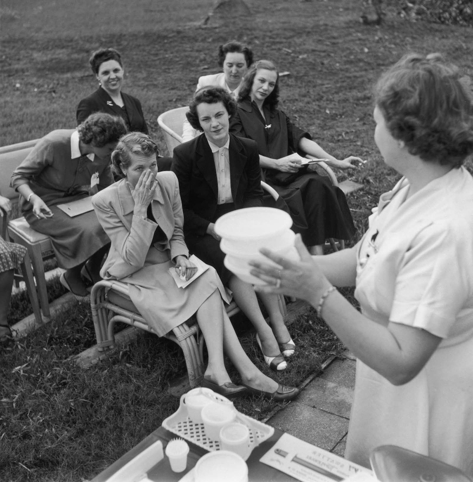 Women attend a Tupperware party, hosted to market the new brand of plastic containers. 1955.