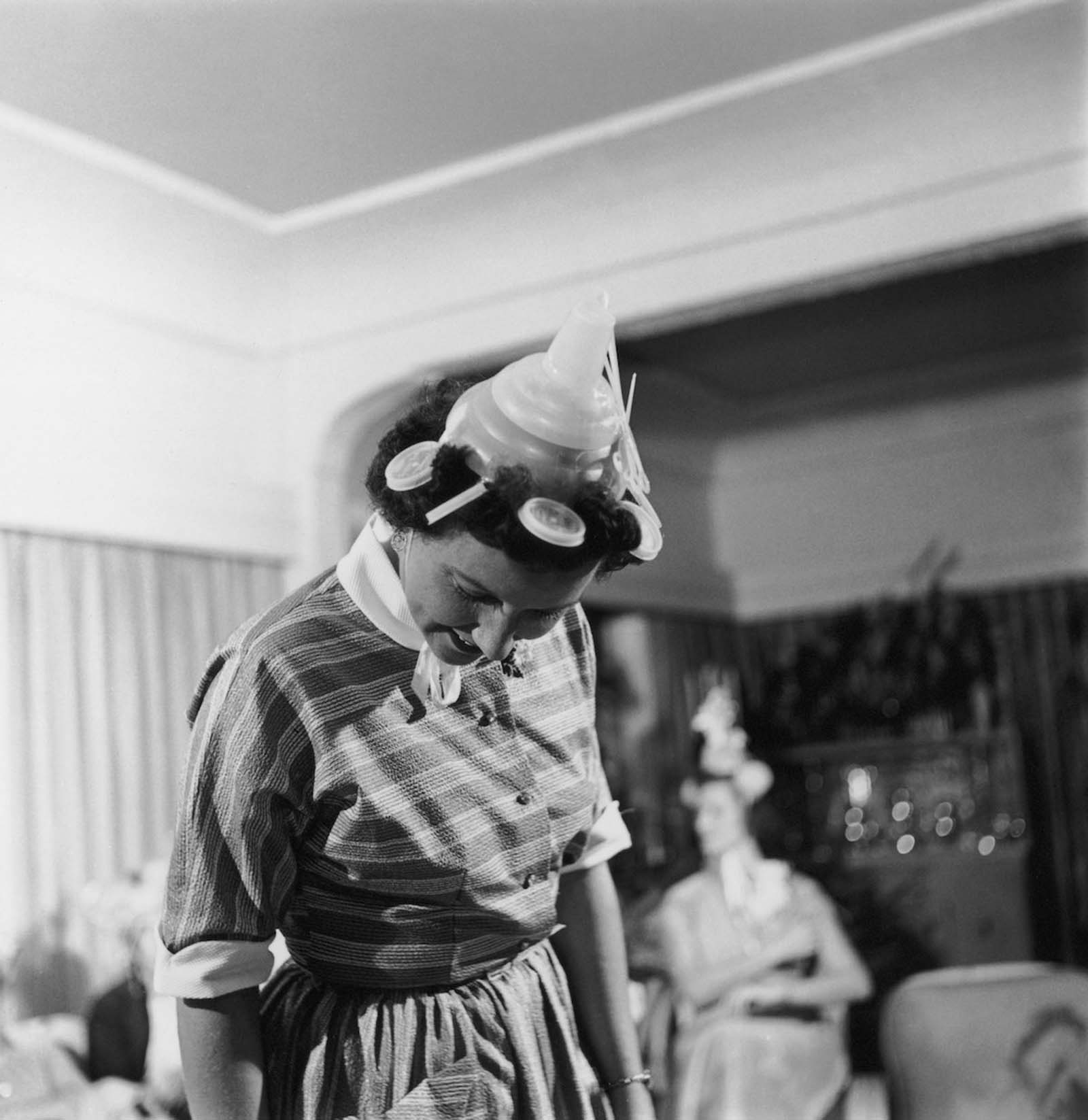 A suitably attired woman attends a Tupperware party. 1955.