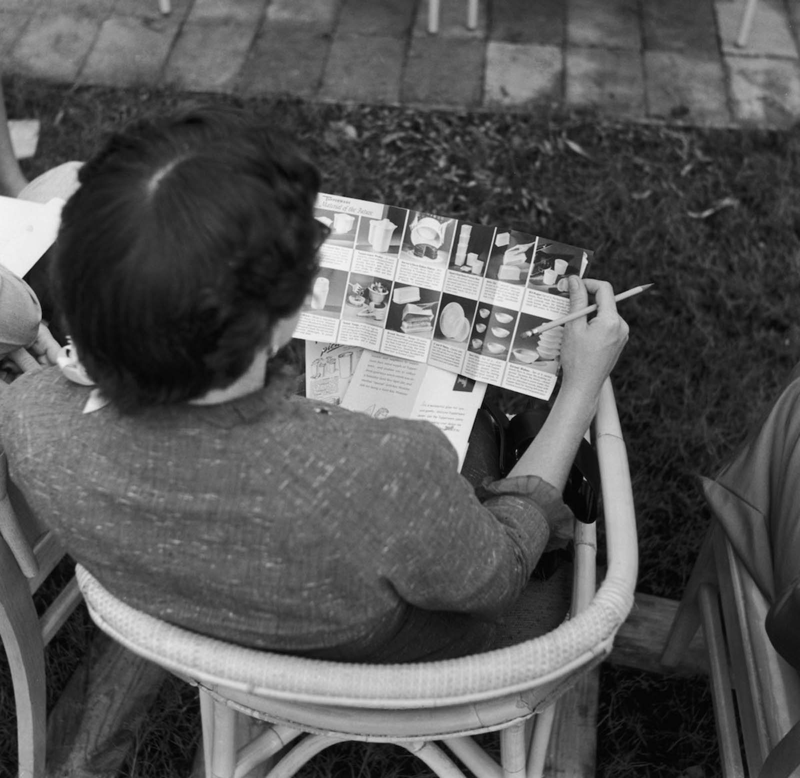 A woman browses the catalogue at a Tupperware party. 1955.